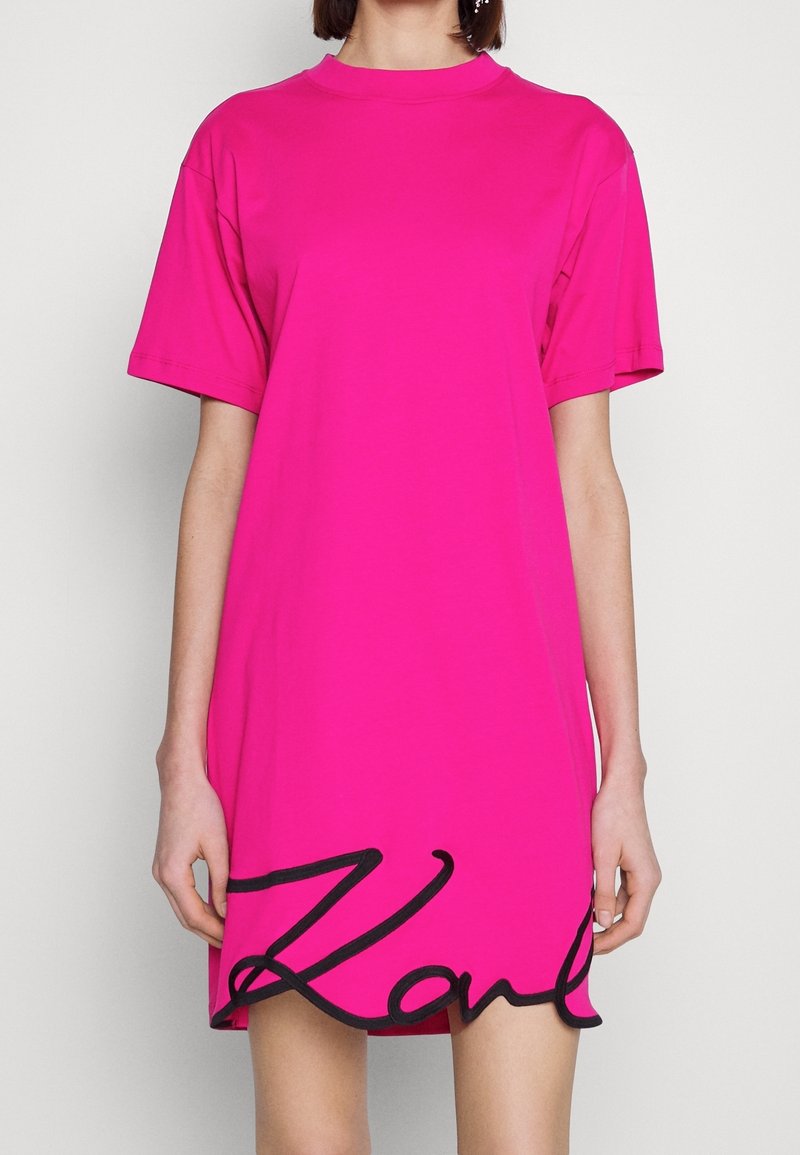 Helles pinkes, übergroßes T-Shirt-Kleid mit kurzen Ärmeln und rundem Ausschnitt. Mit schwarzem, gesticktem "Karl" am Saum. Weiche Textur.