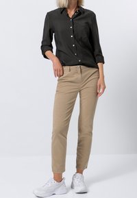 Chemise noire à boutons, chinos beige et baskets blanches. La chemise a un col et une poche ; les chinos sont droits avec une texture lisse.