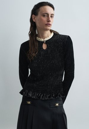 Top negru texturat cu guler în formă de cheie, guler crema cu volane și margine din satin cu volane, purtat cu o fustă plisată neagră cu accente aurii.