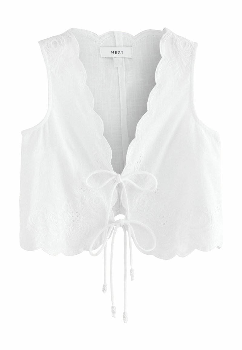 Haut court sans manches blanc avec bords ondulés, broderie florale et fermeture à nouer à l'avant, étiquette "NEXT" à l'intérieur du col.