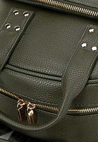 Zaino in pelle verde oliva con hardware dorato, finitura testurizzata, dettagli di cucitura e doppi cursori per le cerniere. Presenta dettagli in borchie sul tamburo.