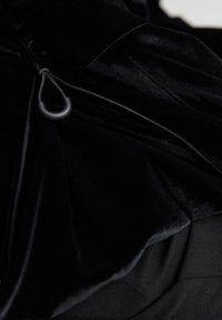 Gros plan sur un tissu en velours noir montrant une fermeture éclair partiellement dézippée avec une languette noire en forme de boucle sur un vêtement.