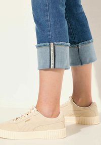 Krémové kožené tenisky s texturovaným povrchem a gumovou podrážkou. Doplněné o srolované džíny z denimu s kontrastním světle modrým manžetovým lemem.