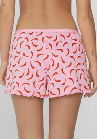 Lichtroze shorts met een herhaald patroon van rode chilipepers. De stof is zacht, met een golvende rand en een elastische tailleband.