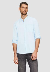 Lichtblauwe shirt met een Chinese kraag, knoopsluiting en opgerolde mouwen. Gemaakt van een gestructureerde stof. G комбинировано met versleten zwarte jeans.