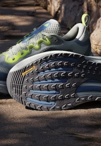 Chaussures de course grises et vertes au sol, montrant une semelle noire texturée avec le logo Continental en extérieur.