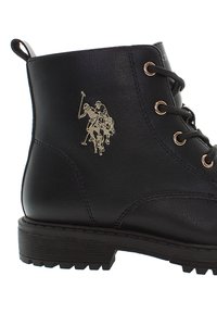 Musta nahkainen nauhoitettava nilkkam derniers kengät, joissa on uurteinen pohja ja kultasävyinen Polo-pelaajan logo sivulla.