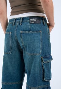 Bermudas de mezclilla en azul oscuro con un ajuste relajado, que presentan grandes bolsillos laterales, costuras en contraste y un parche de marca en la parte trasera.