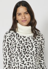 Vit tröja med ribbad polokrage och svart djurmönster, med en mjuk textur och en subtil skimrande effekt.