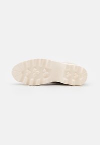Suela de goma blanca de un zapato con patrones de relieve y forma redondeada, que presenta una impresión de logo cerca del talón.