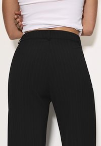 Crne hlače s prugastim uzorkom, s uskim pojasom, koje imaju glatku teksturu i kroj prilagođen tijelu za elegantan izgled.