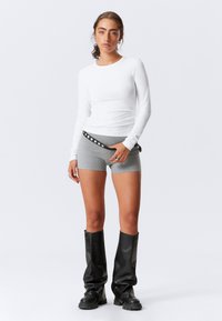 Haut blanc à manches longues associé à un short gris et des bottes noires jusqu'aux genoux. Comprend des ornements en métal argenté sur la ceinture du short.