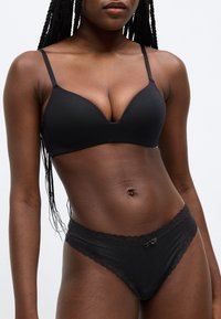 Σετ μαύρου εσωρούχου που περιλαμβάνει ένα λείο, ενισχυμένο σουτιέν με V-σχήμα στο ντεκολτέ και ρυθμιζόμενες τιράντες, σε συνδυασμό με ασορτί σλιπ με δαντέλα.