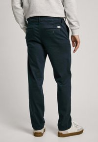 Navy blue cotton pants with two back pockets and button closures, styled with a relaxed fit and paired with white sneakers.
