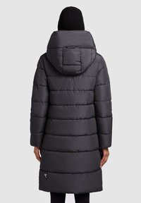 Puhasta jakna tamnosive boje, s kapuljačom, vertikalnim prošivom i dužinom do koljena. Reflektirajući detalj blizu ruba. Glatka tekstura.