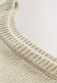 Lichtbeige gebreide trui met een gestructureerde, geribbelde kraag, voorzien van een geweven patroon en een zachte afwerking. Het materiaal lijkt gezellig en ademend.