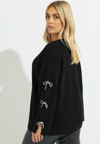 Czarny sweter z dzianiny o teksturowym wykończeniu, z srebrnymi wstawkami na rękawach i luźnym, oversize'owym kroju.