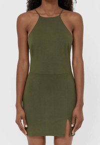 Vihreä oliivinvärinen halterneck-mekko, joka on valmistettu pehmeästä kankaasta ja jossa on istuva muotoilu, kevyt sivuaukko ja ohuet hihnat minimalistista tyyliä varten.