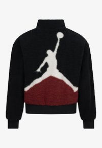 Veste en polaire noire avec une silhouette blanche d'un joueur de basketball et des accents rouges. Les poignets et l'ourlet côtelés viennent compléter le design.
