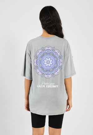 Lys grå oversized t-skjorte med et fargerikt mandala-design og teksten "Beskytt din RO ENERGI" trykket på baksiden.