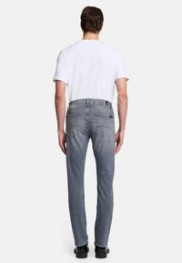 Heren grijze denim jeans met een rechte pasvorm, voorzien van achterzakken en stiksels. Gekleed met een effen wit T-shirt en zwarte schoenen.