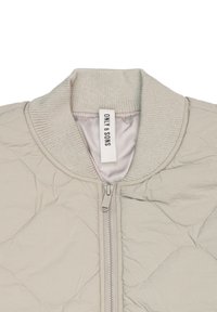 Giacca bomber trapuntata di un beige chiaro con colletto a coste e chiusura con zip. Caratterizzata da cuciture a contrasto e un rivestimento interno liscio.
