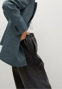 Blazer à carreaux texturé bleu et noir, ouvert à la taille, associé à un pantalon en cuir noir lisse taille haute avec des plis latéraux.