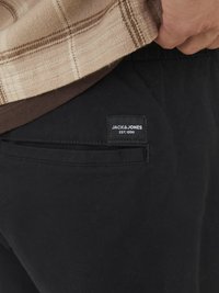 Black pants featuring a back pocket with a rectangular label reading "JACK & JONES EST. 1990." The texture is smooth, with a simple design.