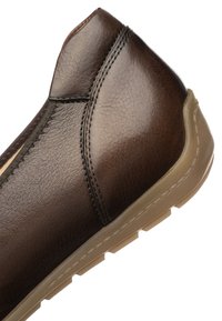 Brown leather slip-on shoe with visible stitching and beige rubber sole angled to show side and heel details.