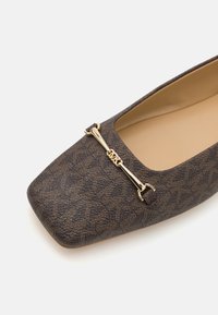 Chaussure plate marron à motif avec un bout carré, surface texturée et un accent en métal doré sur le devant.