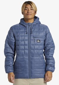Blaue Steppjacke mit Kapuze, Frontreißverschluss, Brusttasche und zwei Seitentaschen. Hergestellt aus leichtem, glänzendem Material mit elastischen Bündchen.