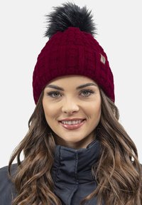 Berretto a maglia bordeaux con un motivo testurizzato e un pompon in pelliccia sintetica nera sulla sommità. Etichetta visibile sul lato.