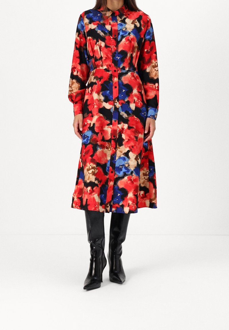 Robe chemise à fleurs rouge, bleu et beige sur fond noir ; manches longues, boutons sur le devant, longueur sous le genou, associée à des bottes noires montantes jusqu'aux genoux.