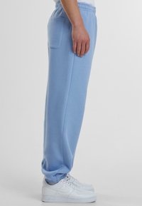 Hellblaue Sweatpants mit lockerer Passform, elastischem Bund, Seitentasche und gerippten Bündchen, kombiniert mit weißen Turnschuhen.