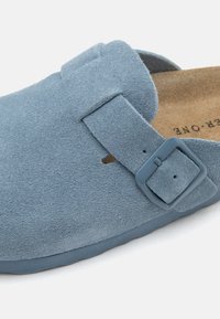 Chaussure slip-on en daim bleu clair avec une bride réglable et boucle, dotée d'une semelle intérieure en liège moulée et d'un bout arrondi.