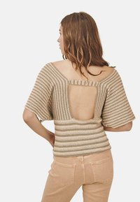 Top de punto beige con mangas anchas y espalda descubierta, que cuenta con una pequeña tira horizontal. Combinado con jeans ajustados de color claro.