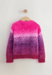 Puchaty sweter z długim rękawem w poziome paski w odcieniach różu, fioletu i czerwieni, wiszący na drewnianym wieszaku na tle białej ściany.
