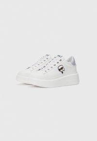 White sneakers with a smooth leather finish, purple accents, round toe, flat platform sole, and a graphic logo patch on the side.