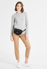Sort bæltetaske båret over en grå sweater, parret med beige bukser og hvide sneakers. Sweateren har en rund halsudskæring og ribbede manchetter.