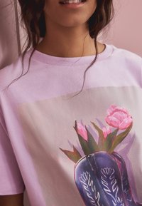 Light purple cotton t-shirt featuring a floral print with pink tulips in a dark blue vase. Soft texture, crew neck design.