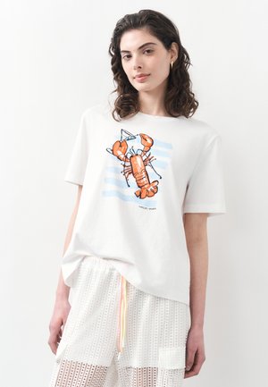 Joven con cabello oscuro y ondulado, lleva una camiseta blanca con un gráfico de una langosta naranja y pantalones cortos blancos de malla con un cordón colorido.