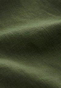 Olivenfarvet stof med en struktureret overflade, der viser et subtilt vævemønster og en blød, mat finish. Stoffet fremstår let og falder blødt.