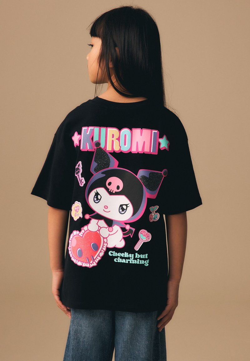 Bambino con capelli lunghi e neri indossa una maglietta nera Kuromi con personaggio dei cartoni animati, testo colorato e la frase "Birichino ma affascinante."