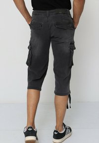 Shorts cargo jusqu'aux genoux en denim gris foncé, dotés de poches latérales, d'une coupe décontractée et d'ourlets retroussés. Portés avec des baskets noir et blanc.