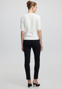 Maglione bianco a maniche corte e pantaloni neri aderenti. Il maglione ha una consistenza liscia, mentre i pantaloni sono eleganti con una vestibilità su misura.