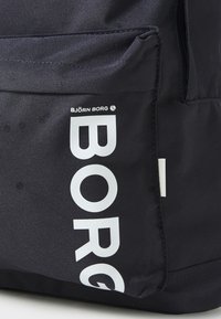 Črn nahrbtnik iz blaga z belim logotipom "BORG" in oznako "BJÖRN BORG". Ima teksturirano površino in stransko žep.