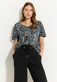 Top de manga corta en blanco y negro con patrón de hojas abstractas, con escote en V y corte relajado, combinado con pantalones negros holgados.