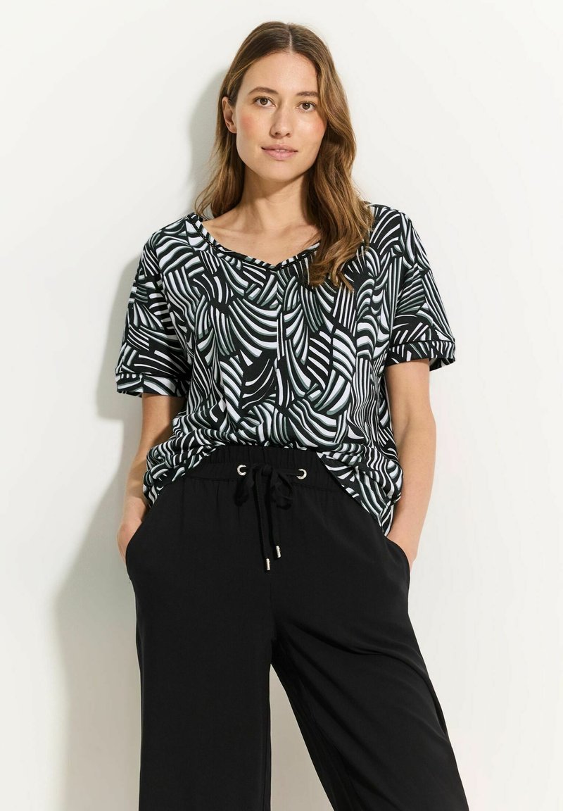 Top de manga corta en blanco y negro con patrón de hojas abstractas, con escote en V y corte relajado, combinado con pantalones negros holgados.