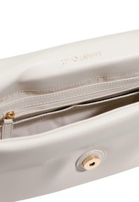 Bolso de cuero beige claro con textura suave. Cuenta con un cierre de botón dorado y un bolsillo interior con cremallera. Grabado sutil de la marca en el interior.