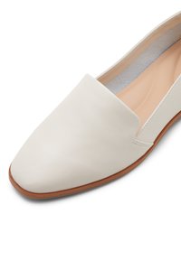 Valkoinen nahkainen slip-on-kengä, jossa on terävä kärki ja ohut ruskea pohja. Sisäpuolella beige vuori. Saumapistot ulko- ja sisäpuolella.